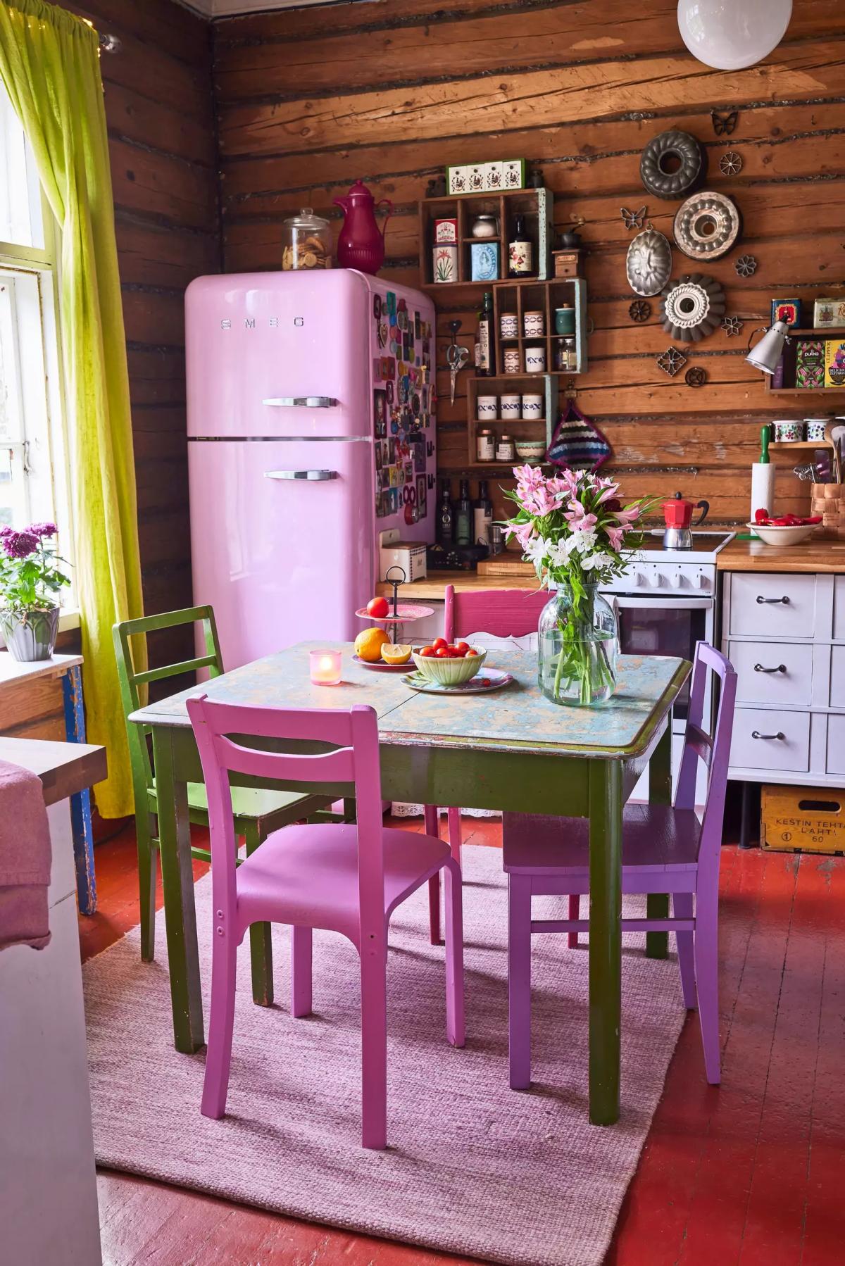 Kitchen with a pink Smeg fridge, a vintage table, and colorful chairs