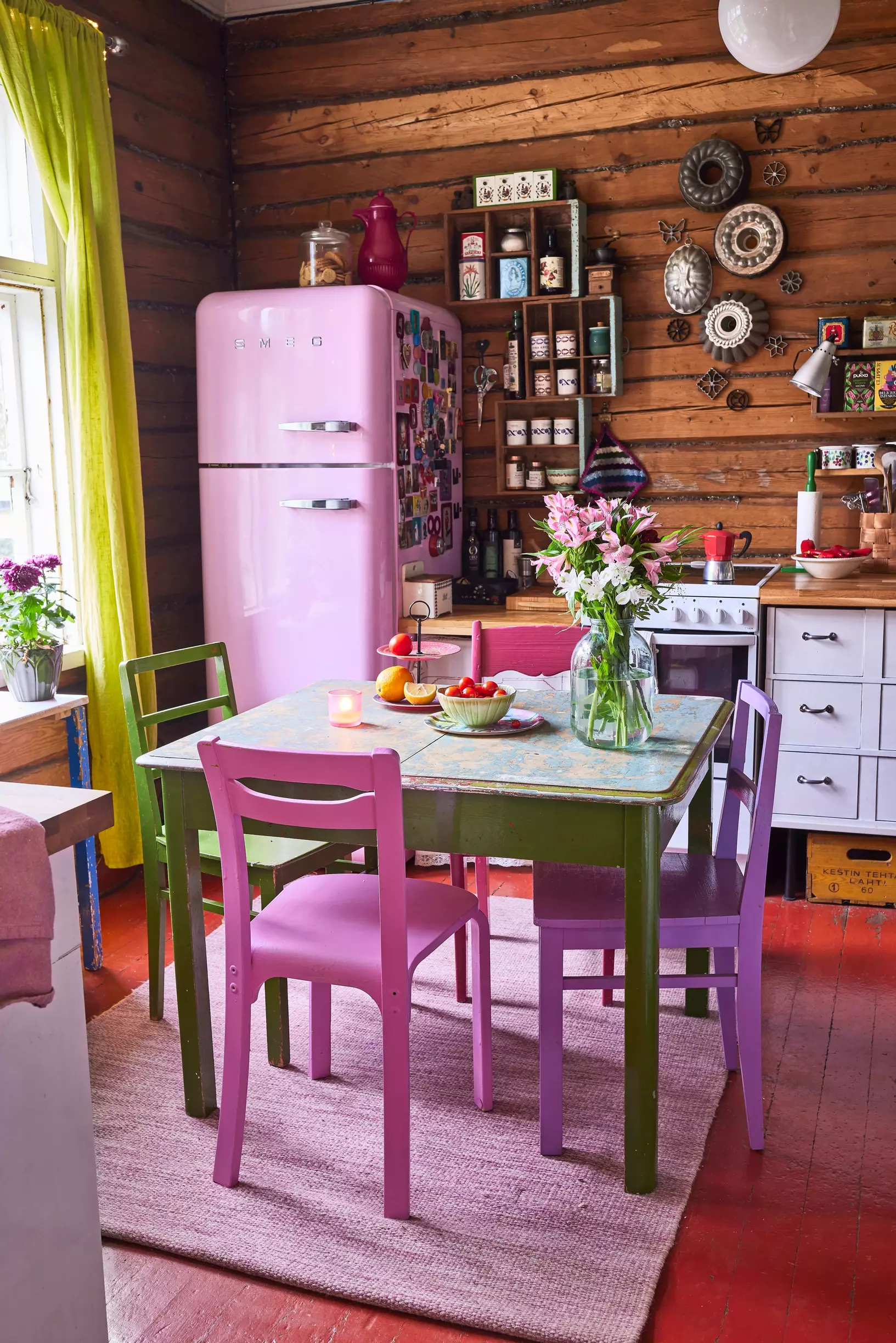 Kitchen with a pink Smeg fridge, a vintage table, and colorful chairs